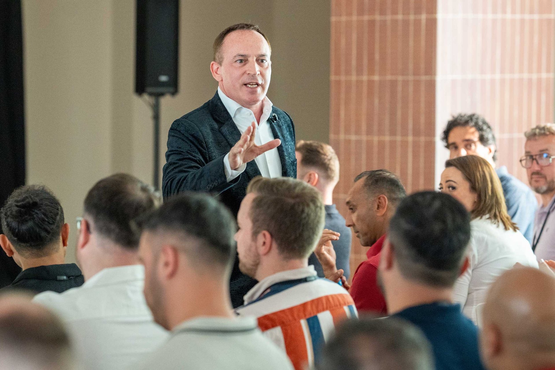 Man in business suit speaking to a diverse audience gathered indoors during a professional presentation or conference event